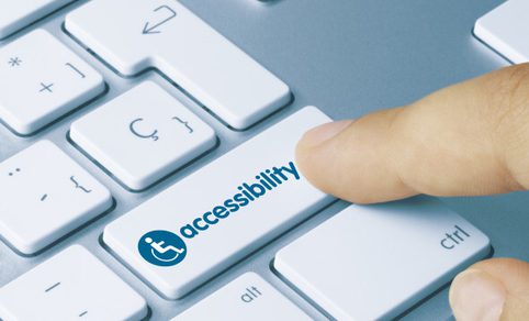 A finger presses a computer keyboard key labeled ‘Accessibility,’ shown with a universal accessibility icon.
