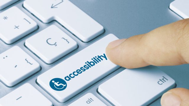 A finger presses a computer keyboard key labeled ‘Accessibility,’ shown with a universal accessibility icon.