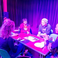 5 people gathered around a table in the boiler house with purple haze lighting.