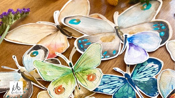 Colourful hand-painted paper butterflies scattered across a wooden table.