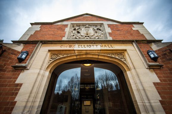 Picture of the entrance to the Elliott Hall. It has modern sliding doors that open when you approach it, dark red brick and words carved above the door reading 'THE ELLIOTT HALL'