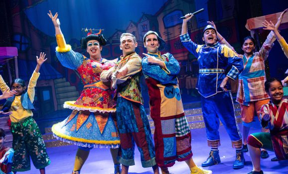 A group of actors performing on stage in elaborate costumes depicting a pantomime.