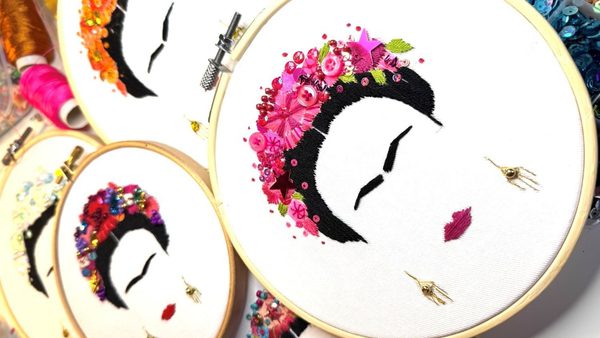 Three embroidery hoops showing an embroidered face of Frida Kahlo with pink, red and orange flowers