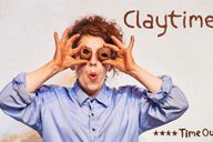 A lady wearing a blue shirt, holds 2 clay 'eyeballs' to her face, with a surprised expressed#! The show title 'Claytime' is displayed proudly on top of a 4 star review from Timeout.