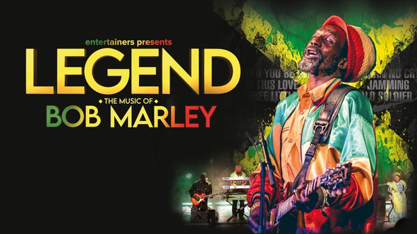 Tribute to Bob Marley, the artist stands on the right, wearing a green and orange jacket and orange hat. He plays guitar and sings. the title of the show, 'Legend, the music of Bob Marley' is on the left in yellow, green and red letters.