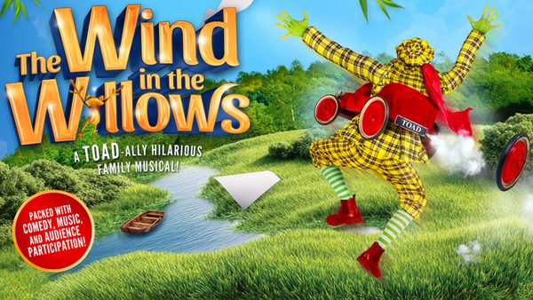 An image of a beautiful green landscape with a river and little wooden boat in the distance. The character of Toad faces away from the camera, jumping for joy towards the greenery. Toad is wearing a yellow tartan suit, red boots and has a red car. The show title, Wind in the Willows, is displayed in big god letters in the top left hand corner.