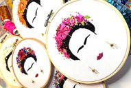 Three embroidery hoops showing an embroidered face of Frida Kahlo with pink, red and orange flowers