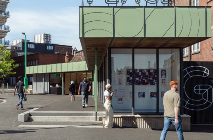 Small green kiosk-style building with large glass windows displaying artwork, set in a modern urban plaza.
