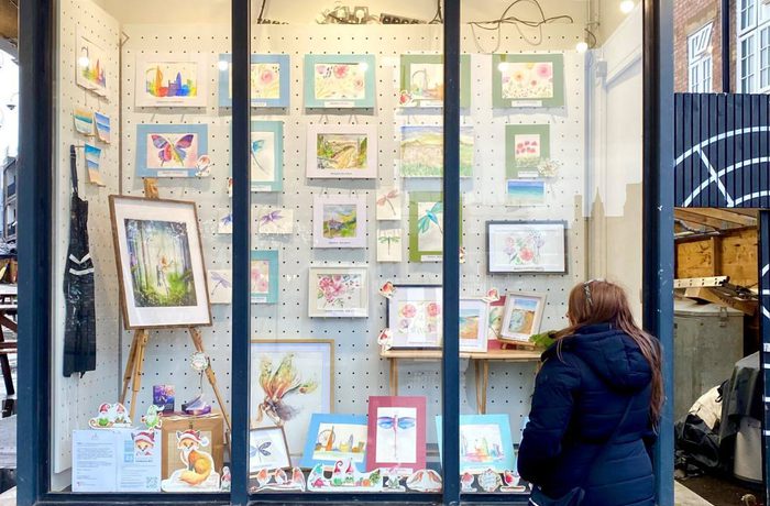 Art and paintings displayed behind a clear window. Woman from outside looks at the paintings.