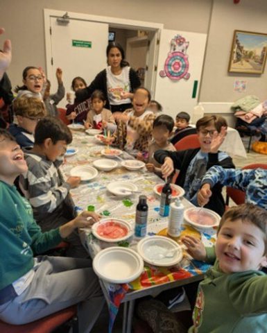 Kids smile and wave as they are sat around a table doing arts and crafts.