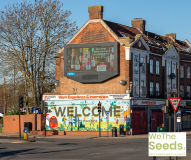 A 'Welcome' mural on the side of a building on a busy street.