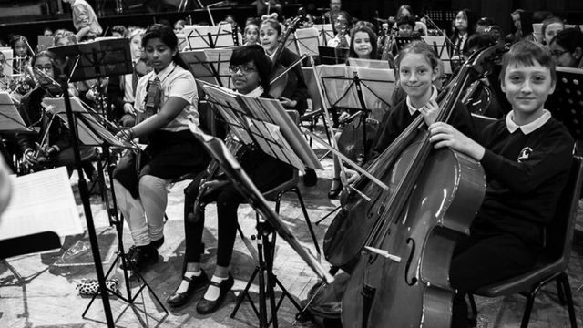 Black and White photo of children in an orchestra posing their instruments.