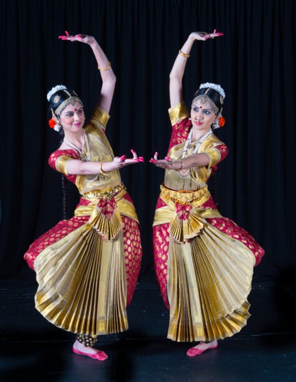 Two women in traditional Indian clothing do a dance pose facing each other