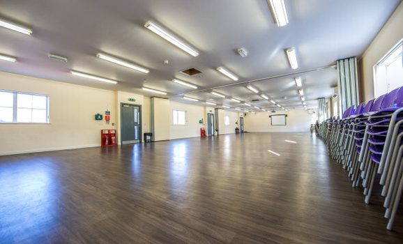 Large empty room with chairs stacked up on the right hand side.