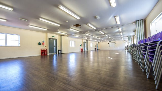 Large empty room with chairs stacked up on the right hand side.