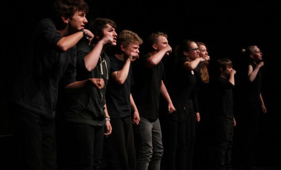 A row of young people in black t-shirts performing on stage.