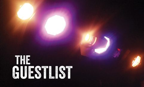 Out of focus close up of Stage Lights shining orange and purple light against black background with white text in the bottom left corner reading 'The Guestlist'