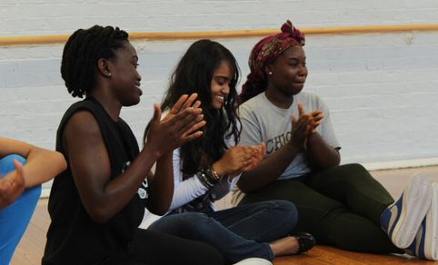 3 Young Women clapping their hands and smiling whilst looking to the right.
