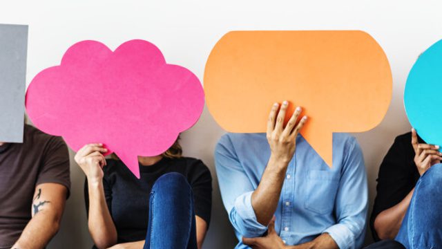 Four seated people hold colourful speech-bubble shapes in front of their faces, representing feedback or opinions.