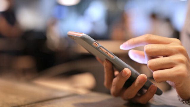 A person holds an iphone with the light of the screen shining on their hand.