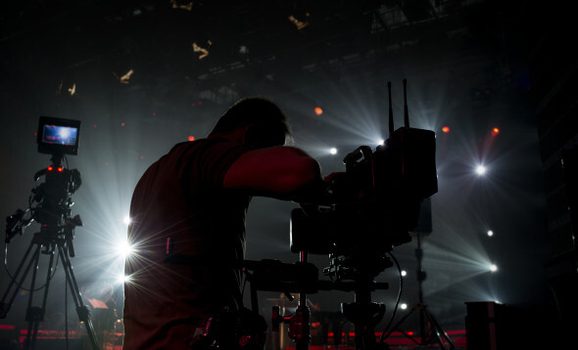Dark lighting with a man standing and filming with camera.