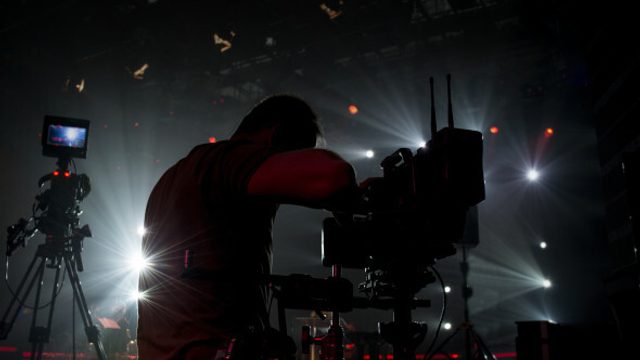 Dark lighting with a man standing and filming with camera.