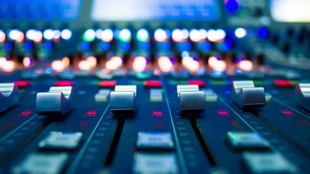 Close-up of an audio mixing console with multiple faders and glowing LED indicators, shot with shallow depth of field and blue-toned lighting.