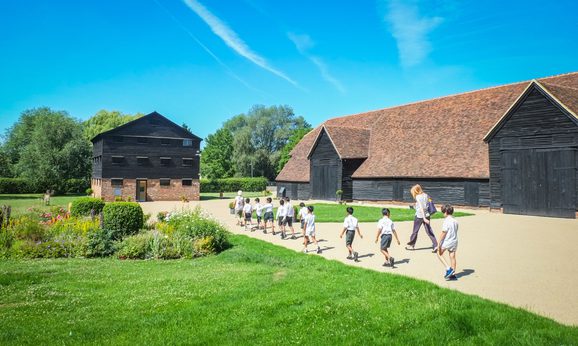 A group of school children and their teacher walk across the path that leads to the granary