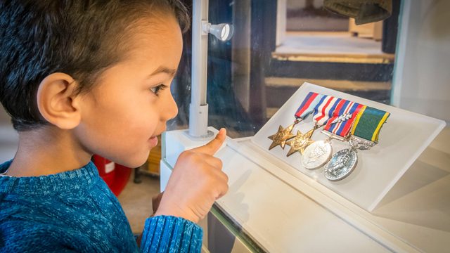 Boy looks at World War 2 medals that are on display behind clear glass