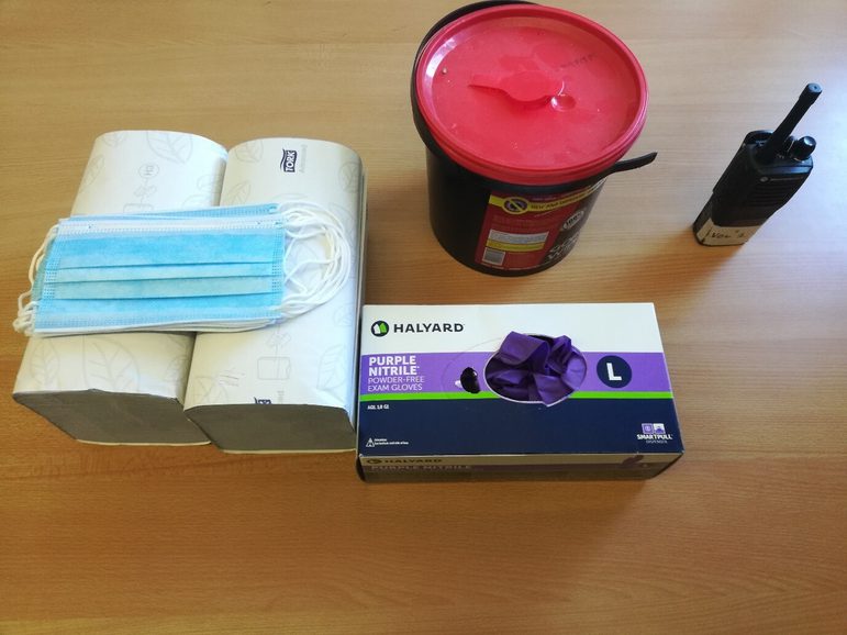 Collection of personal protective equipment on a wooden table, including: disposable facemask, disposable gloves, blue paper towels and others