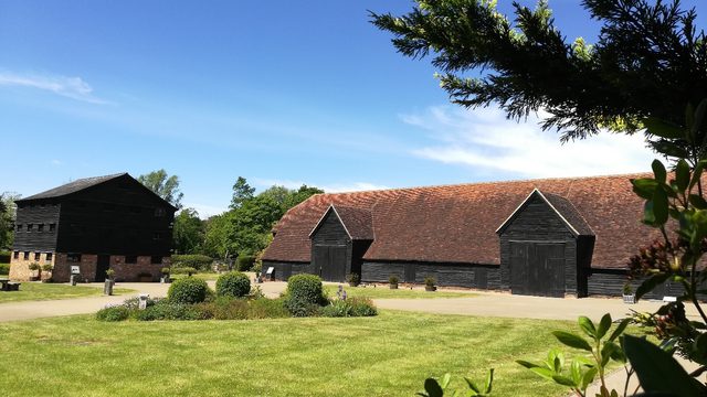 The courtyard of Headstone Manor and Museum in summer, green grass, the granary building and the great barn in the background.