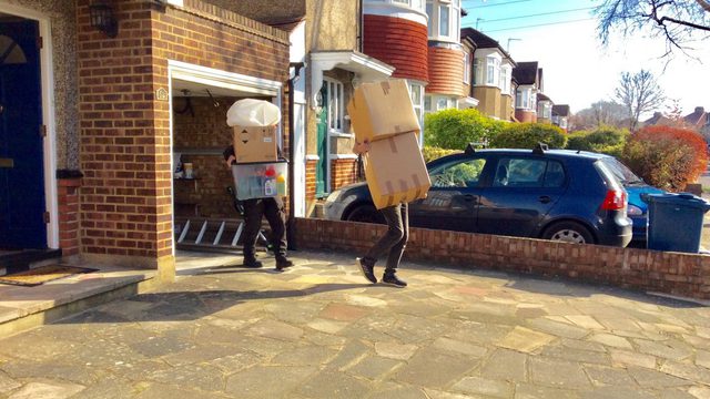 Two people carrying moving boxes from a garage of a house
