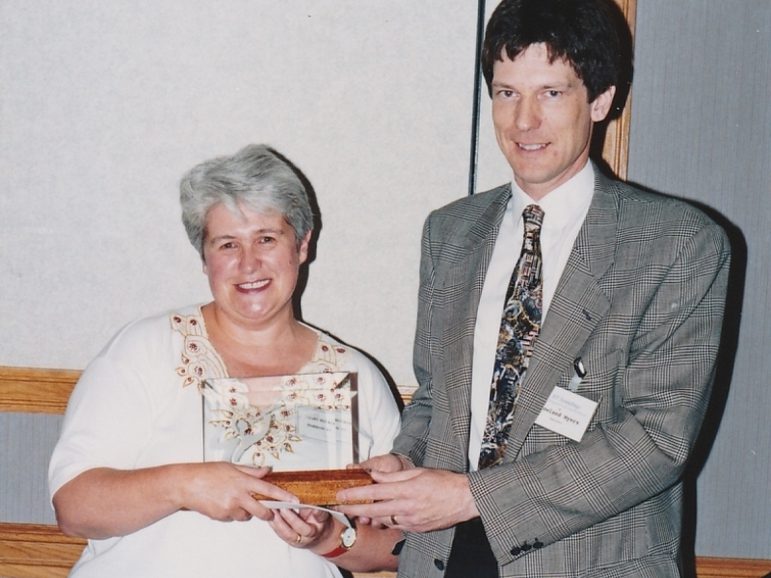 A woman accepting an award from a man with a grey blazer and tie.