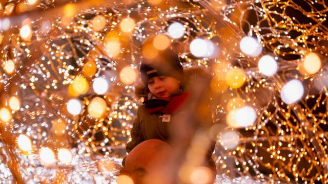 Young child sat on their parents shoulders surrounded by glowing lights
