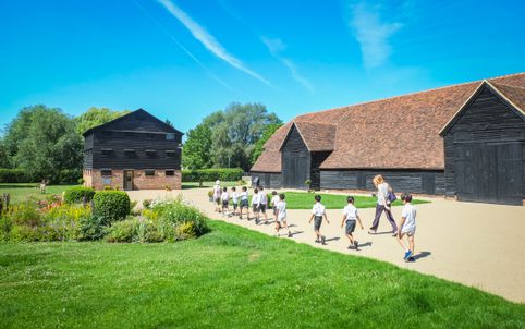 Schoolchildren walking in a line towards a two storey barn for a learning session with Headstone Manor and Museum