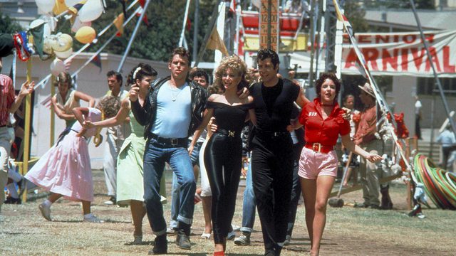 An image from the film 'Grease' of Sandy, Danny and their friends walking through a carnival.