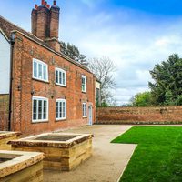Photo showing manor house, large wooden planters and a green space.