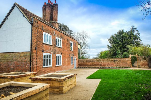 Photo showing manor house, large wooden planters and a green space.