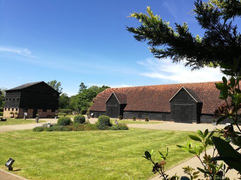 A wide angle shot with grass in the foreground and 2 old buildings in the background, 1 being the barn and 1 being the gallery.