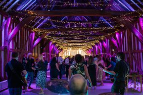 Guests dance and mingle on the dancefloor beneath purple lighting and fairy lights