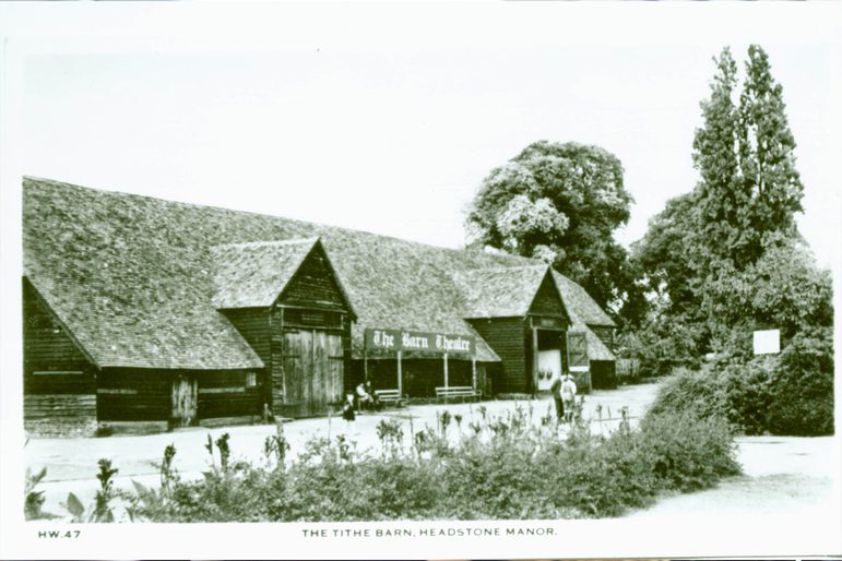 A black and white image of the barn with trees and shrubs surrounding it